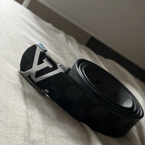 Svart rutigt bälte med silverdetaljer - Säljer ett snyggt svart bälte med ett diskret rutigt mönster. Bältet har en stilren silverfärgad spänne som ger en lyxig känsla. Perfekt för att piffa upp vilken outfit som helst, oavsett om det är till vardags eller fest. Bältet är i nyskick och redo för en ny ägare!