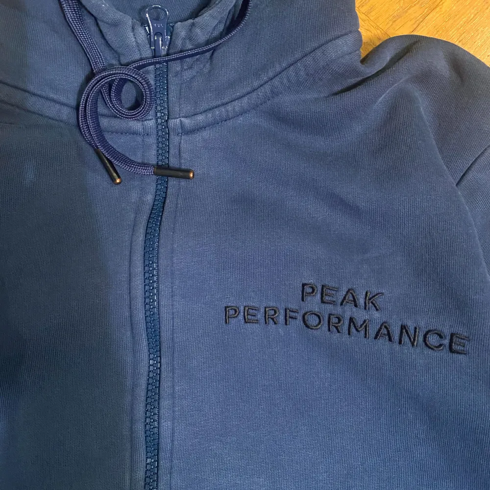 Säljer en snygg blå hoodie från Peak Performance. Den har en dragkedja framtill och en justerbar huva med snören. Perfekt för en avslappnad stil och passar bra till både vardag och träning. Storlek Medium . Hoodies.