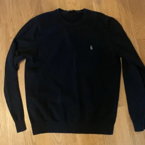 Svart tröja från Ralph Lauren - Säljer en stilren svart tröja från Ralph Lauren. Den har en klassisk design med långärmade ärmar och en liten broderad logga på bröstet. Perfekt för både vardag och lite finare tillfällen. Tröjan är i bra skick och redo för en ny ägare!