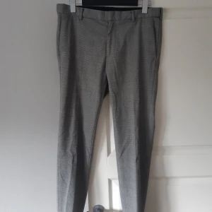 Grå rutiga kostymbyxor från H&M - Säljer ett par stiliga grå kostymbyxor från H&M i storlek 32. Byxorna har ett klassiskt rutmönster och en skinny fit som ger en modern look. Perfekta för både kontoret och festligare tillfällen. Endast använda 2-3 gånger och redo för en ny ägare!