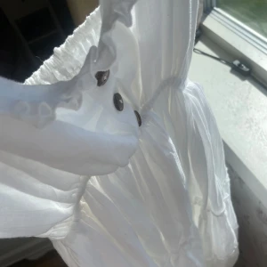 Vit långklänning med knappar - Säljer en superfin vit klänning med knappar framtill. Klänningen har en luftig och somrig stil med volanger vid axlarna och en vacker struktur i tyget. Perfekt för sommarens alla fester eller en avslappnad dag på stan! Aldrig använd