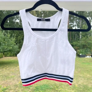 Crop top - En vit crop top från Bikbok. Har en randig kant längst ner med blått, vitt och rött. Säljer den pga att den är lite för liten 💙❤️🤍 Sparsamt använd!  Längd: 37 cm Axel: 22 cm Midja: 63 cm