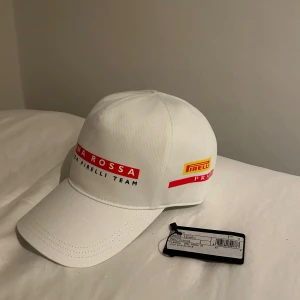 Prada keps - En häftig collab mellan Prada och Luna Rossa Pirelli Team. Kepsen är stilren vit keps med respektive märke på båda sidor av kepsen. Storlek S och den är endast testad!