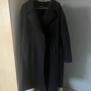 Svart kappa från Gina Tricot - Snygg svart kappa från Gina Tricot i klassisk stil. Perfekt för höst och vinter med sin eleganta design och långa ärmar. Kappan har en stilren look med krage och är i mycket bra skick. Passar både till vardags och festliga tillfällen.