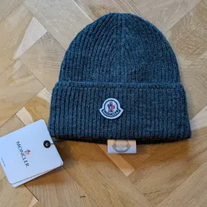 Säljer en snygg grå ribbad mössa från Moncler. Den är i nytt skick och har en broderad Moncler-logga framtill. Perfekt för att hålla sig varm under höst och vinter. Mössan är gjord av mjukt material som känns skönt mot huden. Säljes billigare pga ej kvitto finns!