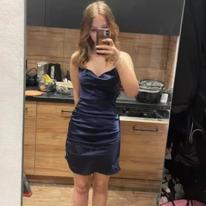 Mörkblå axelbandslös klänning - Säljer en elegant mörkblå axelbandslös klänning i satin. Perfekt för festliga tillfällen med sin figurnära passform och glansiga yta. Klänningen har en kort längd och en stilren design som framhäver figuren. Passar perfekt för en utekväll eller en speciell fest!