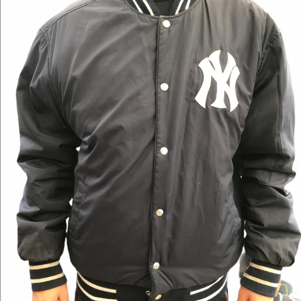 Säljer en sällsynt vintage svart bomberjacka från Jeff Hamilton med New York Yankees-logga. Jackan har långa ärmar och knappar framtill. Den är gjord av polyester och läder, perfekt för höst och vår. Den är även reversible så man kan ha den på två sätt!                                                                    Yankees-märke på ärmen och text på ryggen ger en sportig look. Passar perfekt för casual outfits!  Perfekt för collectors!. Jackor.