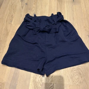 Mörk blå shorts från BikBok - Säljer ett par snygga mörk blå shorts från BikBok i storlek 34. De är högmidjade med ett knytband i midjan för extra stil. Perfekta för sommardagar eller en avslappnad festkväll. Materialet känns mjukt och bekvämt.