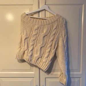Beige stickad tröja - Mysig beige stickad tröja med kabelstickat mönster. Perfekt för kyliga dagar med sin varma och bekväma design. Tröjan har en lös passform och långa ärmar, vilket gör den idealisk för både höst och vinter. Ett måste i garderoben för den som älskar stickade plagg!