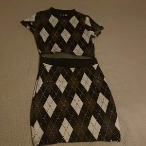 Rutig klänning från Divided - Snygg rutig klänning från Divided i svart och vit med korta ärmar. Perfekt för höst och vår med sitt klassiska mönster. Klänningen har en normal passform och är gjord i ett bekvämt material.