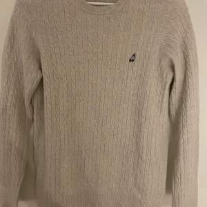 Beige stickad tröja från Peak Performance - Säljer en snygg beige stickad tröja från Peak Performance i storlek L. Den är gjord av fin lammull och har ett klassiskt kabelstickat mönster. Passar både till vardags och lite finare tillfällen samt att ha över en skjorta.