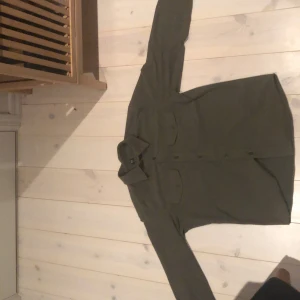 Grön långärmad skjorta - Säljer en stilren grön långärmad skjorta i bra skick. Perfekt för höst och vår, med klassiska knappar framtill. Skjortan har en normal passform och är gjord i ett bekvämt material. Passar både till vardags och lite finare tillfällen.Pris kan diskuteras 