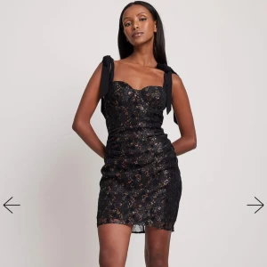 Svart glittrig klänning med rosett - Snygg svart klänning med glittrigt mönster och söta rosetter på axlarna. Perfekt för festliga tillfällen! Den är endast använd en gång!