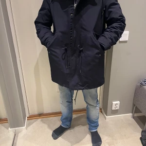 Svart parkajacka - Säljer en svart parkajacka i mycket bra skick. Jackan har långa ärmar och en dragkedja framtill med knappar. Den har en justerbar midja och är perfekt för höst och vinter. Passar både till vardags och lite finare tillfällen. Superbekväm och stilren! 🖤 Storlke M och från arket 