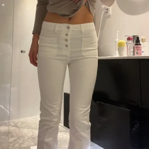 Vita högmidjade byxor - Säljer ett par snygga vita högmidjade byxor i mycket bra skick. De har en tight passform och fem knappar framtill som ger en cool detalj. 