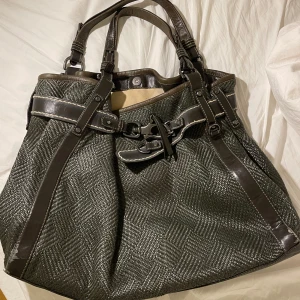 Vintage grå axelväska med läderdetaljer  - Säljer en snygg och rymlig grå axelväska med läderdetaljer. Väskan har ett elegant mönster och flera praktiska fack inuti. Perfekt för både vardag och speciella tillfällen. Den är i mycket bra skick och redo för en ny ägare!