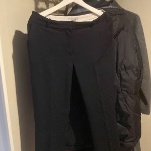 Svarta kostymbyxor från H&M - Säljer ett par stilrena svarta kostymbyxor från H&M i storlek 38. Perfekta för både kontoret och festliga tillfällen. Byxorna har en klassisk passform med raka ben och är tillverkade i ett bekvämt material. De är i mycket bra skick och redo för en ny garderob!