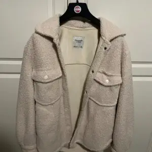 Mysig beige teddyjacka från Abercrombie & Fitch i storlek XS. Perfekt för höst och vinter med sin fluffiga och varma design. Jackan har långa ärmar och knappar framtill, samt två stora fickor på bröstet. Superfin och i mycket bra skick!