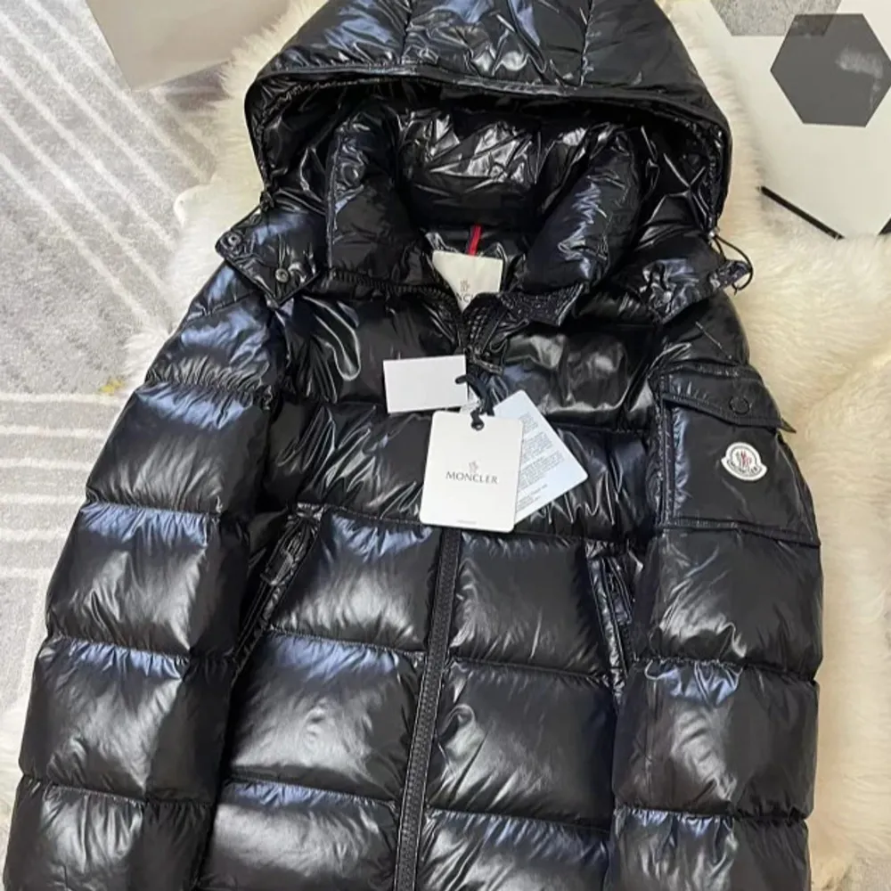 Säljer en snygg svart dunjacka från Moncler i glansigt material. Jackan har en stor huva och dragkedja framtill. Perfekt för kalla vinterdagar. Den är i mycket bra skick och har en cool serietidningsetikett på insidan. Passar perfekt för både vardag och festliga tillfällen.. Jackor.