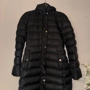 Svart dunjacka med pälskrage från Tommy Hilfiger - Säljer en snygg svart dunjacka med avtagbar pälskrage från Tommy Hilfiger. Jackan har långa ärmar och knappar framtill. Perfekt för kalla vinterdagar. Den är i mycket bra skick och håller dig varm och stilren hela säsongen.
