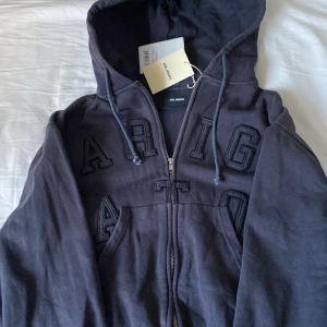 Svart hoodie från Axel Arigato - Säljer en snygg svart hoodie från Axel Arigato i storlek S. Den har en dragkedja framtill och coola bokstäver på bröstet. Perfekt för höst och vår, och den är i nytt skick med taggar kvar. Grym för en casual look! Priset går att diskuteras!