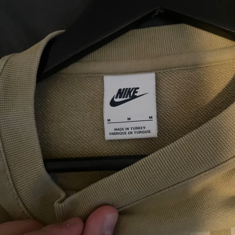 Säljer en snygg beige sweatshirt från Nike i storlek M. Tröjan har en klassisk design med Nike-loggan i vitt på framsidan. Perfekt för en avslappnad stil och passar bra till både jeans och träningsbyxor.. Tröjor & Koftor.