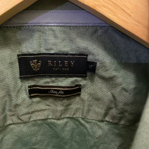 Grön skjorta från Riley - Säljer en stilren grön skjorta från Riley i storlek S. Skjortan har en slim fit passform och är perfekt för både vardag och fest. Den är långärmad med knappar framtill och en klassisk krage. Materialet känns bekvämt och passar bra till både jeans och chinos. Perfekt för vår och sommar! 🌿
