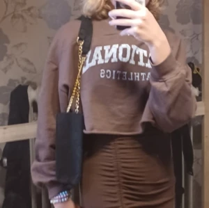 Brun croppad sweatshirt - Säljer en brun croppad sweatshirt med texten 'ATHLETICS' i vitt. Den har långa ärmar och en avslappnad passform, perfekt för en casual look. Passar bra till både jeans och kjol. Perfekt för höst och vår!