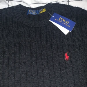 Svart stickad tröja från Ralph Lauren - Säljer en snygg svart stickad tröja från Ralph Lauren i storlek S. Tröjan har ett klassiskt kabelstickat mönster och den ikoniska röda loggan på bröstet. Perfekt för höst och vinter, och den är i helt nytt skick med taggar kvar, aldrig andvänd!