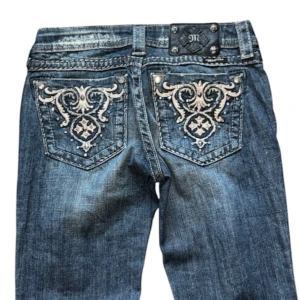 Miss Me Jeans - Snygga blå jeans med unika broderade detaljer på bakfickorna. De har en bootcut-stil som ger en retro vibe. Perfekta för både vardag och fest! Jeansen har en låg midja och är i bra skick. Passar perfekt till en avslappnad eller uppklädd look.