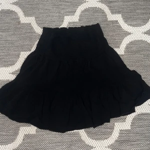 Svart kjol med volang - Säljer en superfin svart kjol med volangdetaljer. Perfekt för både vardag och fest! Den har en elastisk midja för bekväm passform. Kjolen är kort och passar perfekt till sommaren eller en utekväll. 🖤