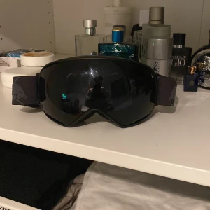 Svarta skidglasögon från Red Bull - Säljer ett par svarta skidglasögon från Red Bull i mycket bra skick. De har en bred, justerbar rem med logotypen och en spegelglaslins som ger ett coolt utseende. Perfekta för vinterns skidäventyr! 🏂