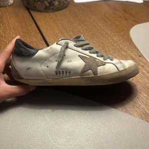 Golden goose  - Säljer ett par goolden goose sneakers. De har en sliten look för en avslappnad stil. Skorna har grå snörning och en bekväm passform. Perfekta för vardagsbruk och att ge din outfit en trendig touch. Riktigt skönt material på insidan vilket gör dem perfekt inför vintern. Storlek 41 men passar 42 hör av er vid minsta fundering :)