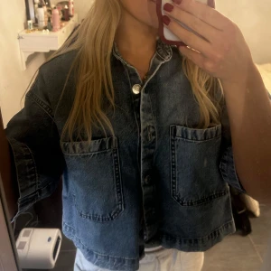 Blå jeansjacka - Säljer en blå denimskjorta i croppad stil med knappar framtill. Den är i bra skick och passar till många olika outfits! Använd en gång