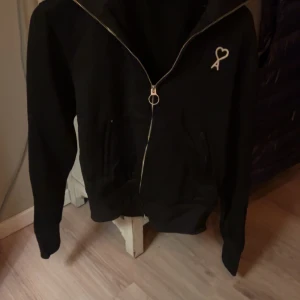 Svart hoodie från Ami  - Säljer en snygg svart hoodie från Ami med en cool broderad logga på bröstet. Den har en dragkedja framtill och är i mycket bra skick. Perfekt för höst och vår, och passar till både vardag och fest. Storleken är S. Hör av dig om du är intresserad!