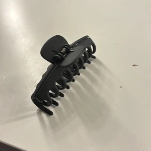 Svart hårklämma - Jag säljer en svart hårklämma i plast med en enkel och stilren design. Perfekt för att hålla håret på plats i en snygg uppsättning. Klämman har en stark fjäder för bra grepp och passar både till vardags och fest.