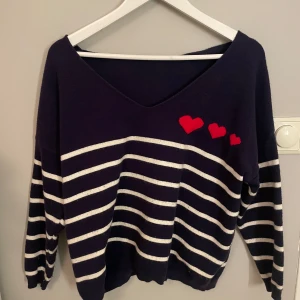 Mörkblå randig tröja från Pinka - Säljer en superfin mörkblå tröja från Pinka med vita ränder och tre röda hjärtan på framsidan. Tröjan har en v-ringad hals och långa ärmar, perfekt för en avslappnad stil. Den är både mysig och stilren, perfekt för höst och vår!