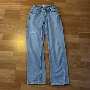 Ljusblå jeans med slitning - Säljer ett par ljusblå jeans i bra skick. De har en snygg slitning på ena benet och en klassisk femficksdesign. Jeansen är raka i modellen och passar perfekt för en avslappnad stil. Perfekta för både vardag och fest!