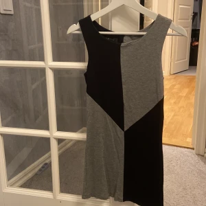 Grå och svart klänning från Amisu - Snygg och stilren klänning från Amisu i grått och svart. Den har en cool geometrisk design och är ärmlös, perfekt för både vardag och fest. Klänningen har en dragkedja på baksidan. Klänningen är i stl 34