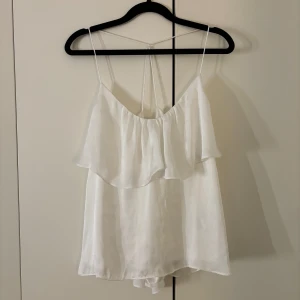 Vit ärmlös topp från Gina Tricot - Ett superfint linne från Gina tricot i storlek 36 (lite liten i storleken). Superfint glansigt material och luftigt. Mycket bra skick då den bara använts några gånger. Finns dock en pytteliten fläck på axelbandet, men inget som syns när man har den på.