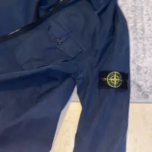 Säljer en snygg blå jacka från Stone Island. Den har en dragkedja och en cool patch på ärmen. Perfekt för vår och höst! Jackan är i bra skick och redo för nya äventyr.