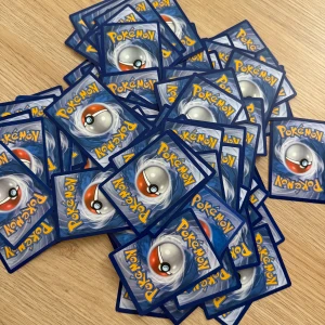 Pokémonkort - En hög med Pokémonkort med den klassiska blå baksidan och en Pokéball i mitten. Perfekt för samlare eller för att spela med vänner. Kortens skick varierar, men de ser ut att vara i gott skick överlag. En kul tillägg till din samling eller för att byta med andra fans! 50 kr för alla 