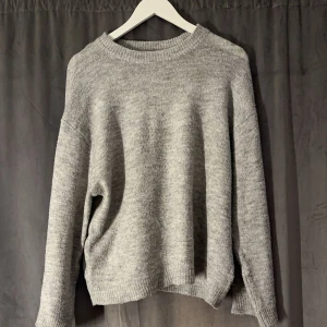 Grå stickad tröja - Mysig grå stickad tröja perfekt för kyliga dagar. Den har en enkel design med rund hals och långa ärmar. Tröjan är i bra skick och passar perfekt för både höst och vinter. Ett måste i garderoben för den som älskar komfort och stil.