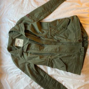 Olivgrön jacka från Hollister - Säljer en snygg olivgrön jacka från Hollister i storlek XS. Jackan har långa ärmar och knappar framtill. Perfekt för höst och vår med sin stilrena design och praktiska fickor. Passar både till vardags och lite mer uppklädda tillfällen.
