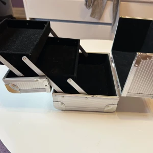 Silverfärgad smink/ smycke väska  med lås - Säljer en praktisk och stilren silverfärgad smink/smycke väska med lås och nycklar. Perfekt för att organisera och förvara ditt smink/ smycken. Väskan har flera utdragbara fack och ett robust handtag för enkel transport. Måtten är ca 17 cm i höjd och 20 cm i bredd. Perfekt för både hemma och resor! 