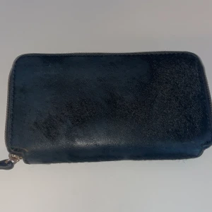 Filippa K Svart plånbok med dragkedja - Säljer en stilren svart plånbok Filippa. K  i skinn med dragkedja,den var pälsig från början , vissa spår av päls finns kvar.Den har flera fack för kort och en praktisk myntficka. Perfekt för att hålla ordning på dina värdesaker. Använd men i bra skick.