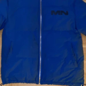 Blå pufferjacka från Mennace - Säljer en snygg blå pufferjacka från Mennace. Jackan har en dragkedja framtill och är perfekt för kyliga dagar. Den är i bra skick och har en cool logga på bröstet och ryggen. Perfekt för höst och vinter!