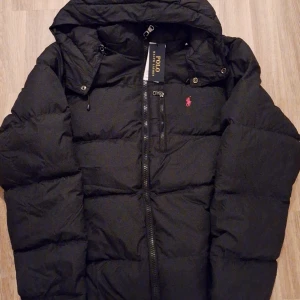 Svart Polo Ralph Lauren puff jacka - Säljer en snygg svart puffjacka från Polo Ralph Lauren i helt nyskick, etiketten sitter kvar. Det finns även en Polo Ralph Lauren påse som ni ser på bilden, den kommer såklart kommer med vid köp. Har ni några frågor eller tankar skriv gärna! Priset är diskuterbart! Jackan är storlek L