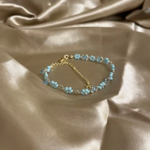 Handgjord Blått blommigt armband med gulddetaljer - Snyggt och delikat armband med små blå blommor och gulddetaljer. Perfekt för att ge en färgklick till din outfit. Justerbar kedja för perfekt passform. Passar både till vardags och festliga tillfällen. Kedjan är gjort av 14k guld pläterad stålfritt stål. 