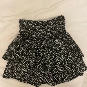 Svart och vit blommig kjol från Zara - Säljer en superfin svart och vit blommig kjol från Zara i storlek 164. Kjolen har en volangdetalj och är perfekt för både vardag och fest. Den är gjord i ett mjukt och bekvämt material som passar perfekt till sommaren. Dessutom har den inbyggda shorts💕
